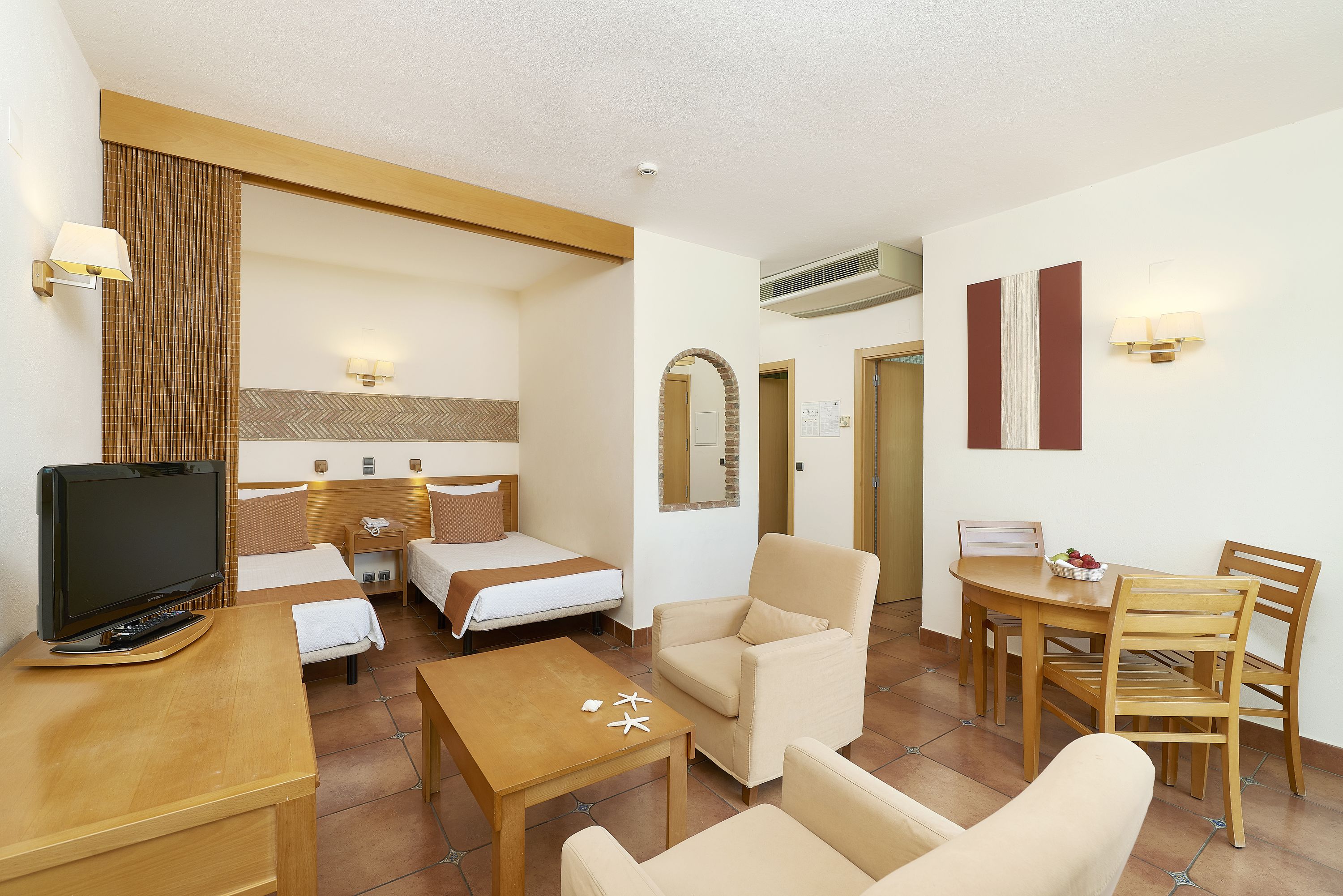 Habitación de hotel con cama, escritorio, televisión, silla, mesa y zona de comedor.