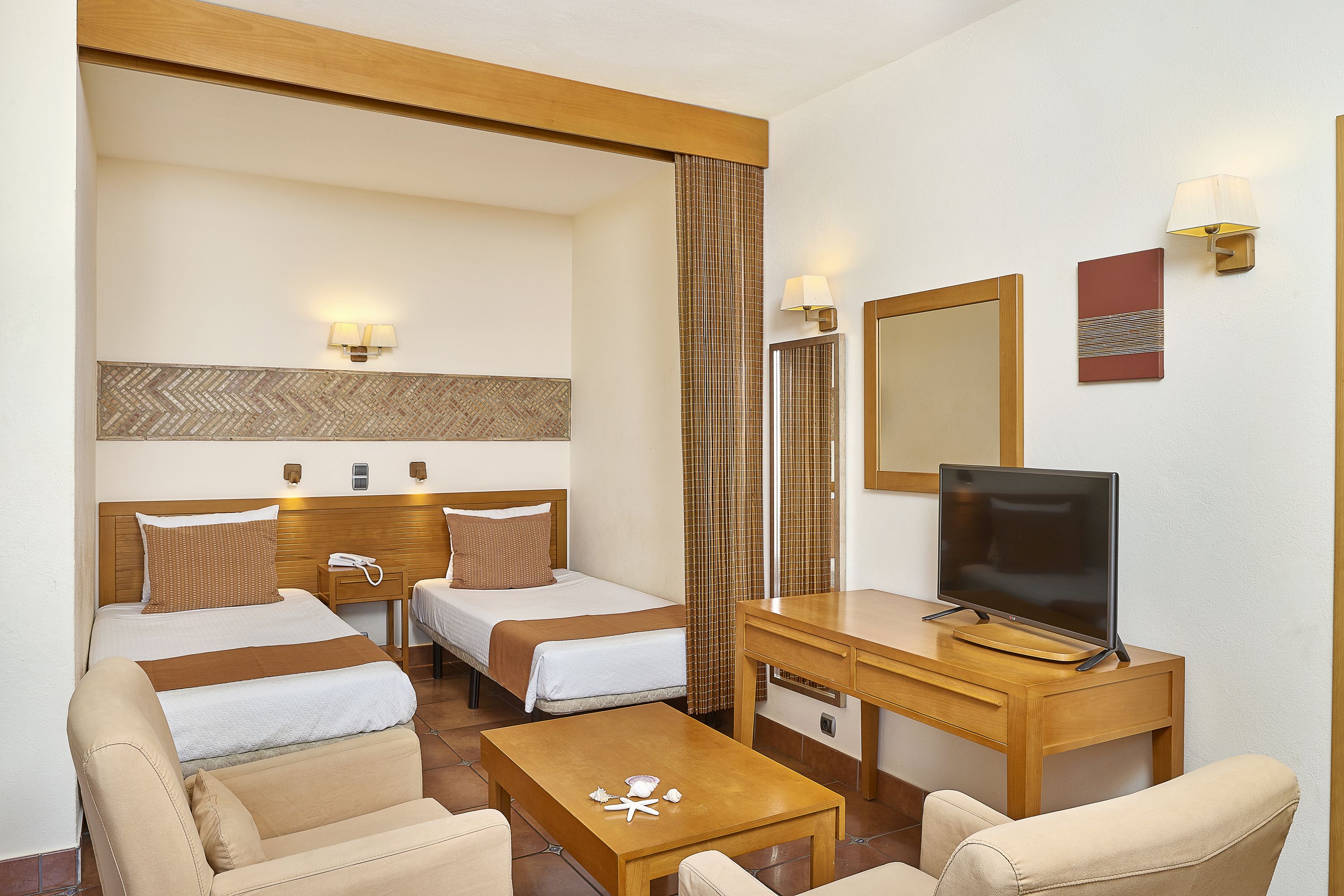 Ett hotellrum med två separata sängar, ett skrivbord med en tv, en stol och ett litet bord.