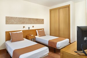 Ένα δωμάτιο ξενοδοχείου με δύο κρεβάτια, μια ξύλινη ντουλάπα, μια τηλεόραση και έναν πίνακα που είναι τοποθετημένος στον τοίχο.