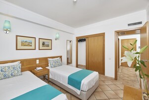 Habitación de hotel con dos camas, una mesita de noche con lámpara, un espejo y cuadros en la pared.
