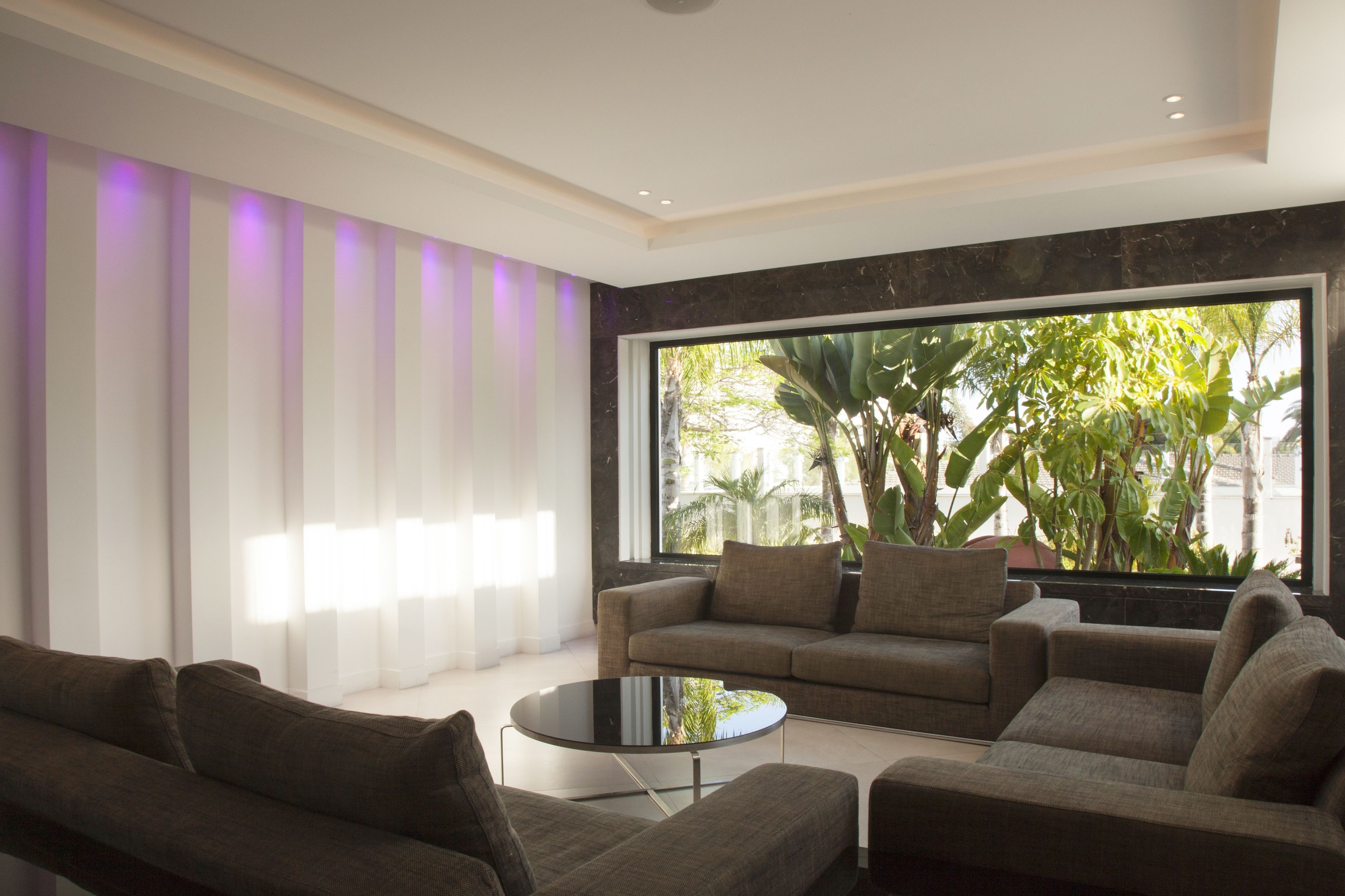 A modern living room with a large window, a sofa, a coffee table, and a striped wall.