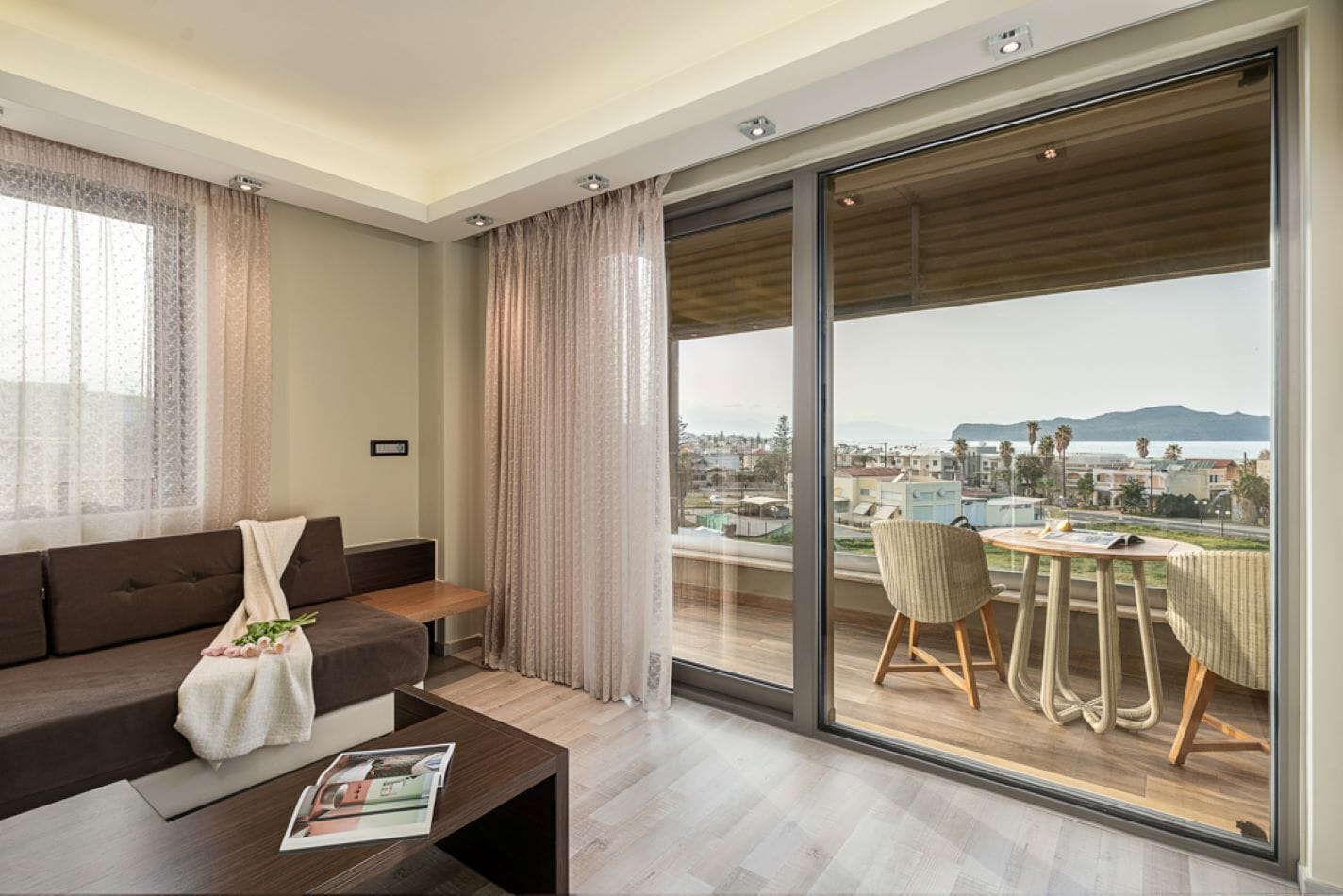 Un salon moderne avec un canapé, une table basse et une vue sur le paysage urbain, visible à travers de grandes portes vitrées.