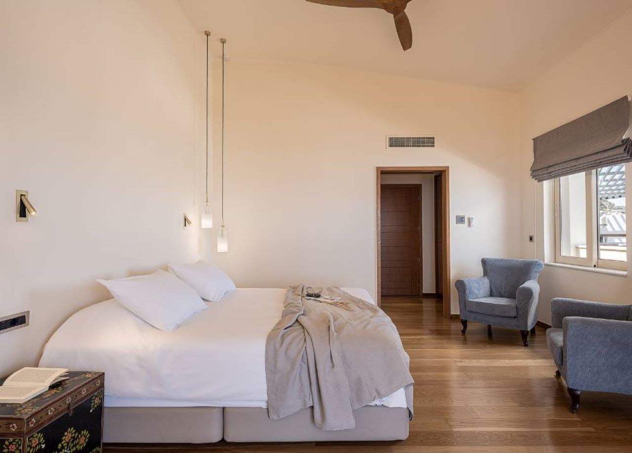 A bedroom with a bed, bedside table, and a chair. There is a door leading to another room.