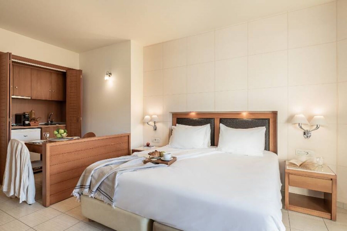 Una habitación de hotel con cama, mesitas de noche, escritorio y kitchenette.