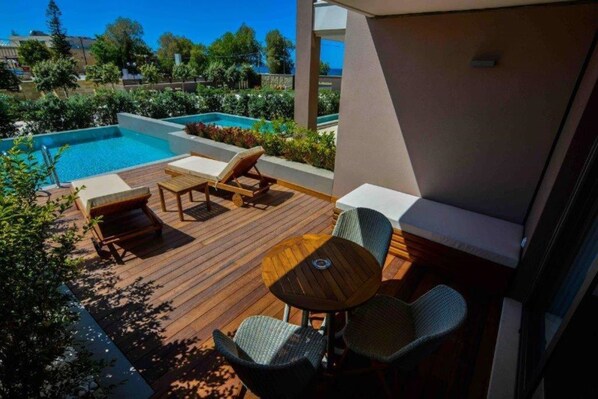 A wooden deck with lounge chairs and a table, overlooking a swimming pool and greenery. - Cretan Dream Resort and Spa (Chania)