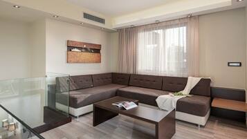 Een moderne woonkamer met een modulaire bank, een glazen salontafel en een groot raam met gordijnen.
