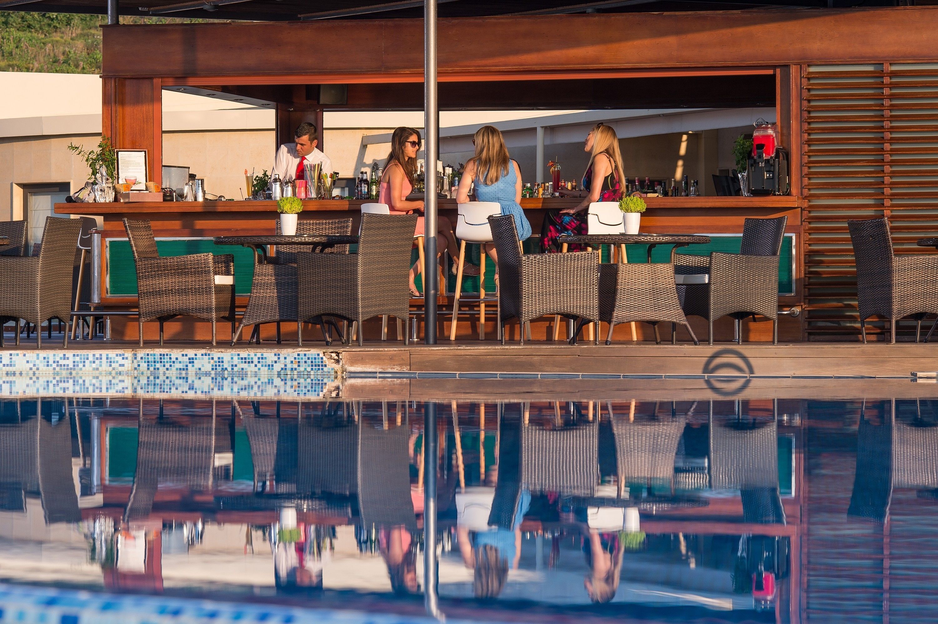 Zona de bar junto a la piscina, con sillas de mimbre y barra.