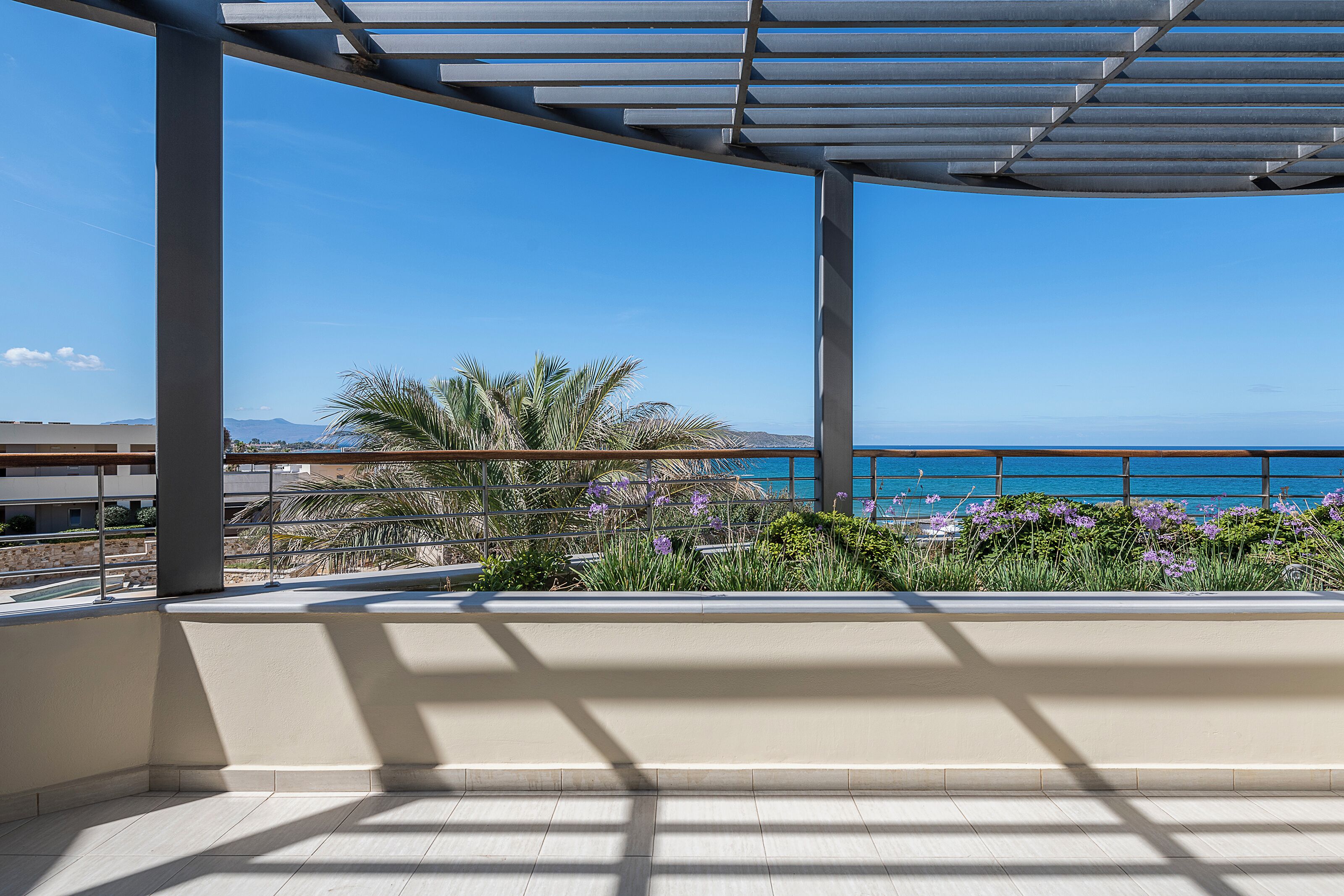 A balcony with a view of the sea, a pergola, and some plants.