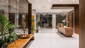 Un área de recepción moderna con un mostrador de madera, plantas en macetas y un separador de vidrio.