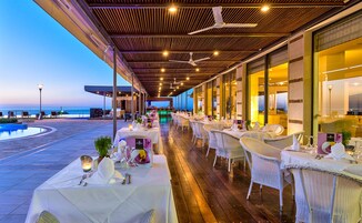 Un área de comedor al aire libre con mesas preparadas para una comida, con vista a una piscina y al océano.