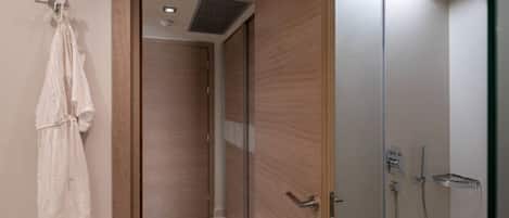 A modern bathroom with a walk-in shower, a wooden door, and a white robe hanging on the wall.