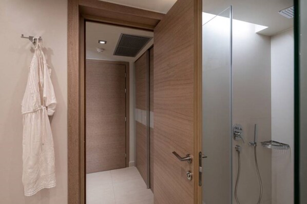 A modern bathroom with a walk-in shower, a wooden door, and a white robe hanging on the wall. - Cretan Dream Resort and Spa (Chania)