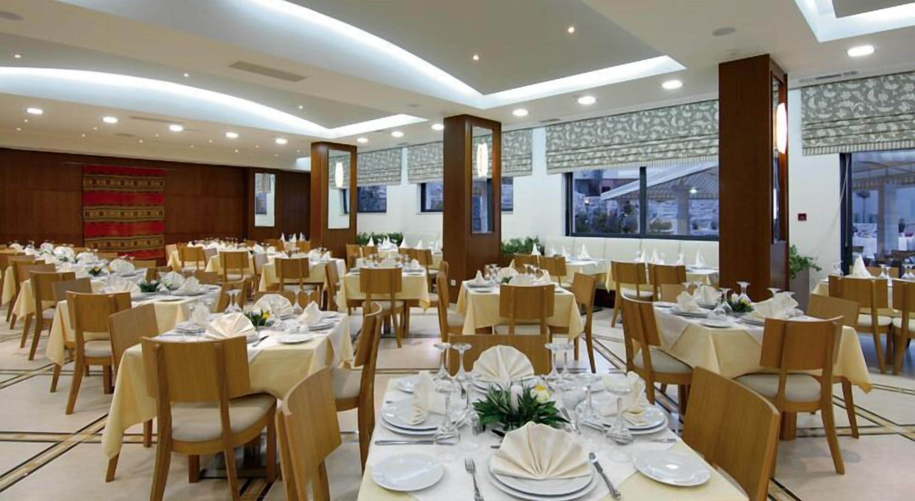 A banquet hall with round tables set for dining, featuring a high ceiling and large windows.