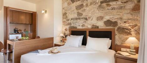 A hotel room with a stone wall, a wooden bed, a desk with a chair, and a nightstand with a lamp.