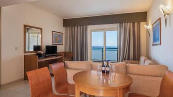 A modern hotel room with a balcony, a sofa set, a dining table, and a TV.