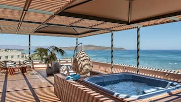 A rooftop terrace with a hot tub, lounge chairs, and a view of the sea.