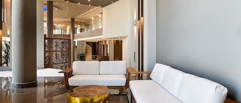 A modern lobby with a white sofa, a gold ottoman, and wooden furniture.