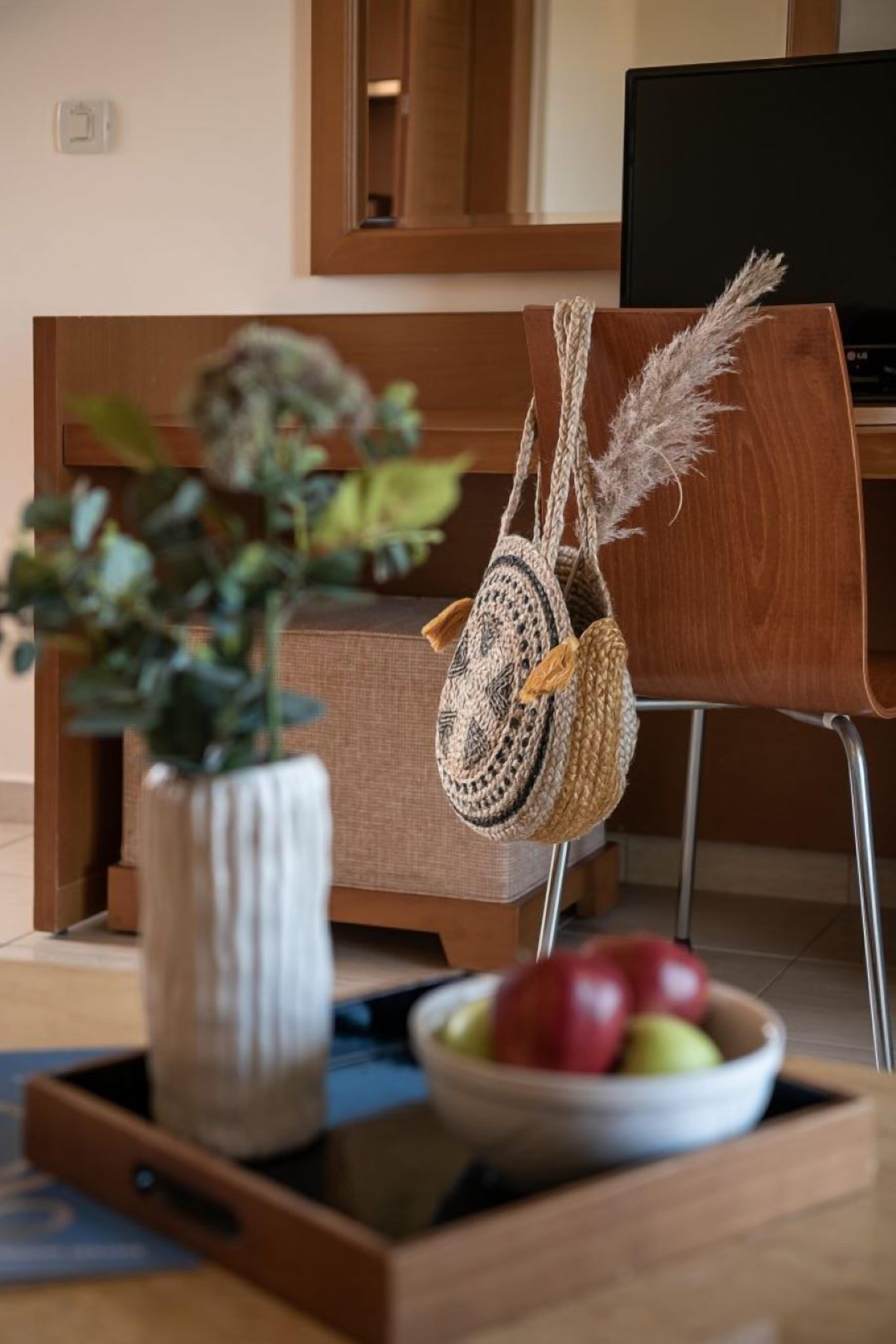 Una silla de madera con un bolso tejido colgando, un cuenco de fruta y una planta en maceta sobre una bandeja.