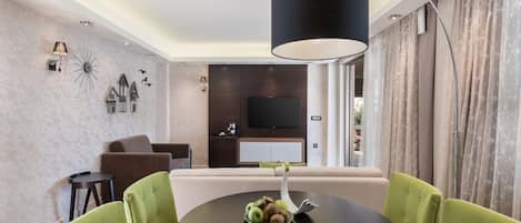 A modern dining area with a round table, green upholstered chairs, and a black lamp.