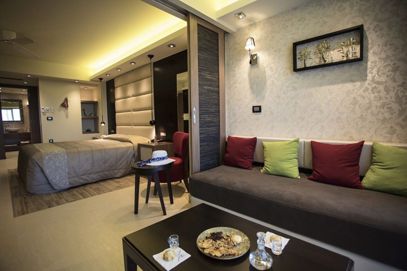 A modern hotel room with a bed, a sofa, a small table with a plate of food, and a chair.