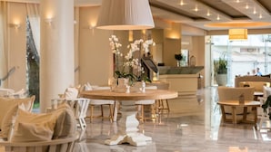 A modern hotel lobby with a round dining table, comfortable seating, and a large central light fixture. - Nefeli Hotel (Rethymno)
