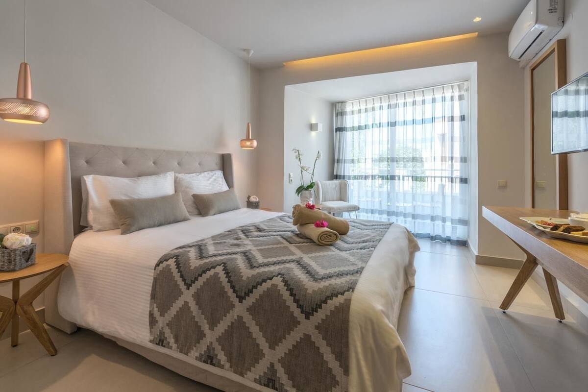 A modern bedroom with a large bed, a bedside table, a chair, and a view of a balcony with curtains.