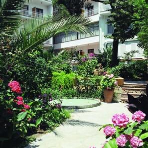 A garden with a circular fountain, surrounded by lush greenery and flowering plants. - Hotel Clipper (Lloret de Mar)
