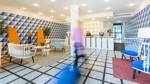 A modern lobby with geometric patterned walls, a reception desk, and seating areas with a mix of white and blue chairs.