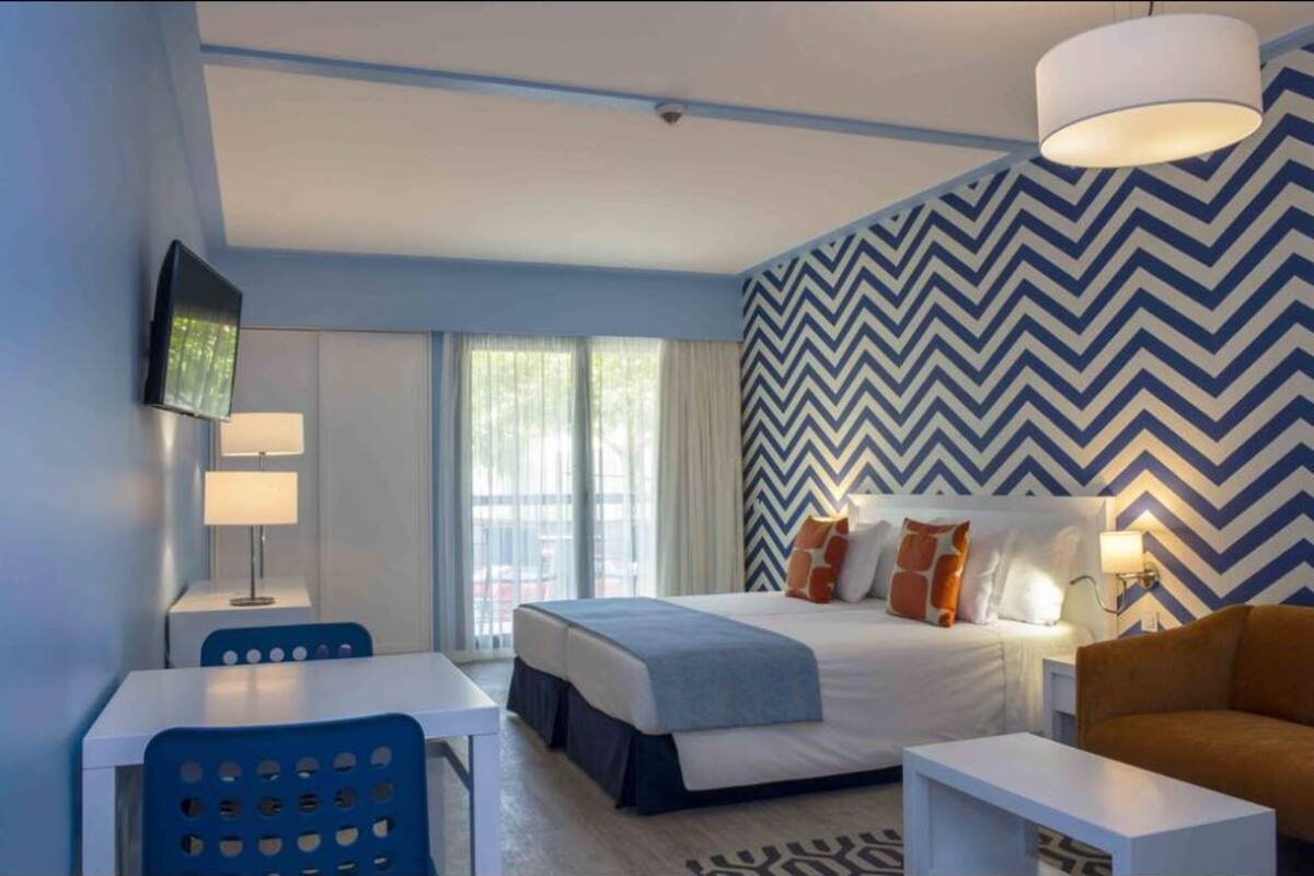 A modern hotel room with a bed, a desk, a chair, and a television.