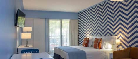 A modern hotel room with a bed, a desk, a chair, and a television.