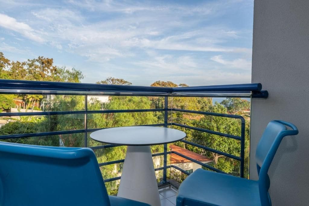 Un balcon avec une table et des chaises, offrant une vue sur la verdure et les bâtiments.