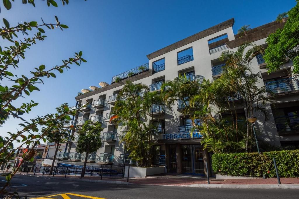 A multi-story hotel with balconies, a terrace, and palm trees.