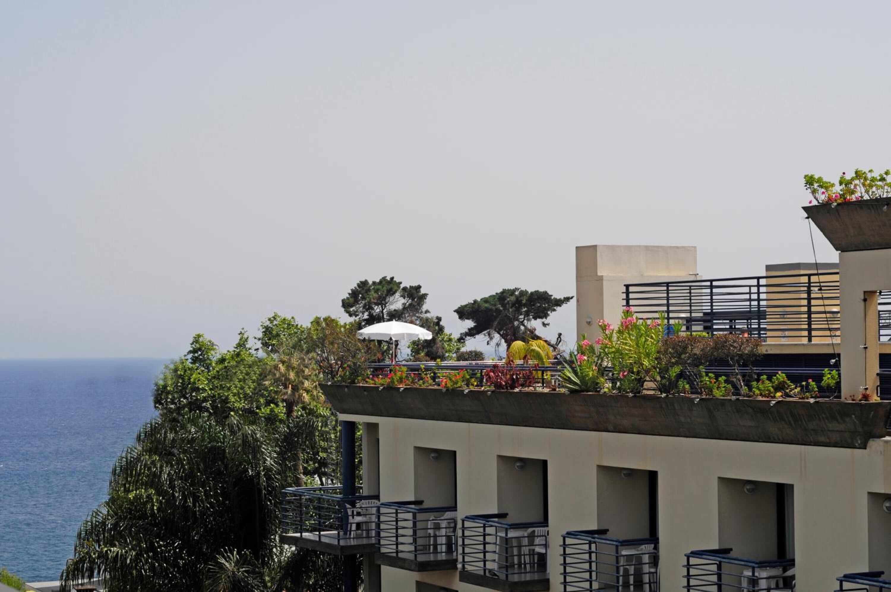 Eine Dachterrasse mit Sitzgelegenheiten im Freien, Blick aufs Meer und einem Blumentopf.