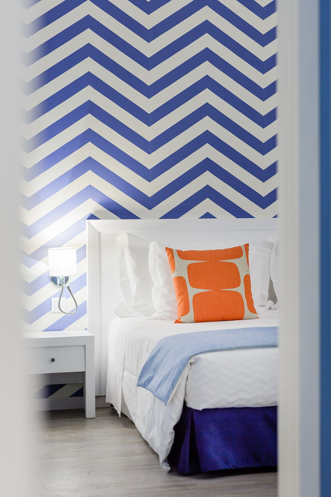 A bedroom with a bed, white nightstand, and a wall with a blue and white chevron pattern.