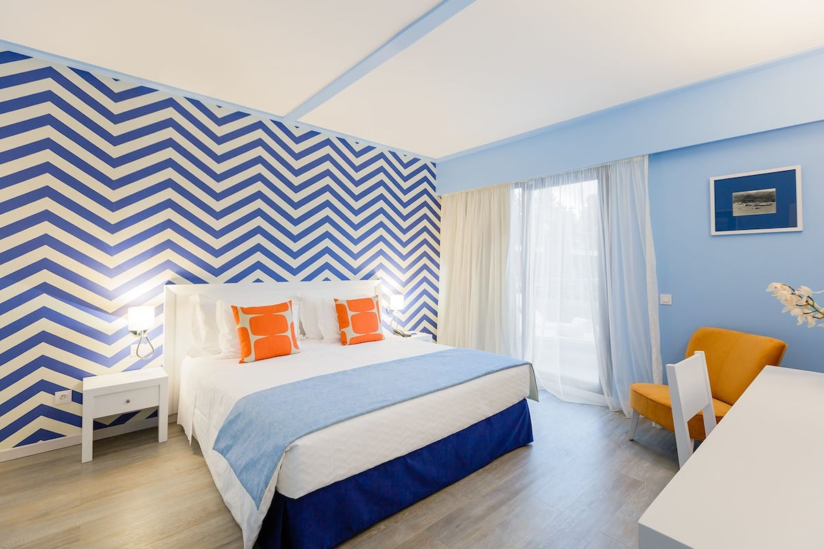 A modern bedroom with a large bed, a nightstand, an orange chair, and a desk.