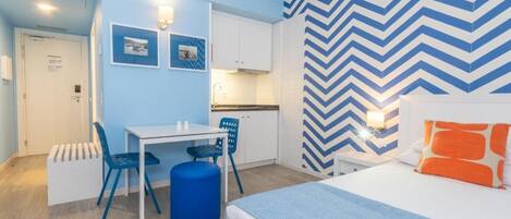 A compact hotel room with a bed, a desk, and a kitchenette.