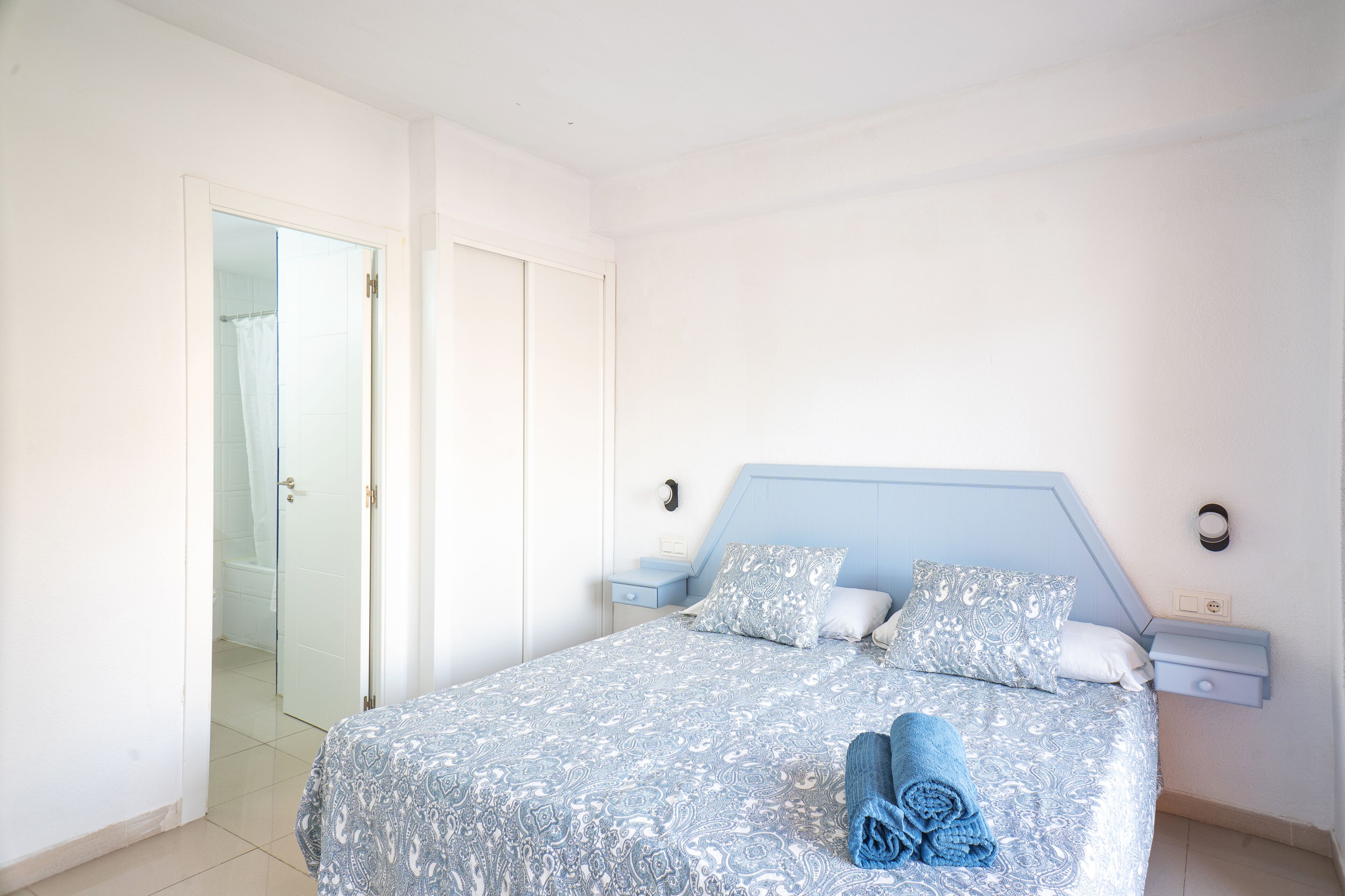 Una camera da letto con un letto, due comodini, un tavolo da notte, una porta del bagno e un asciugamano sul letto.