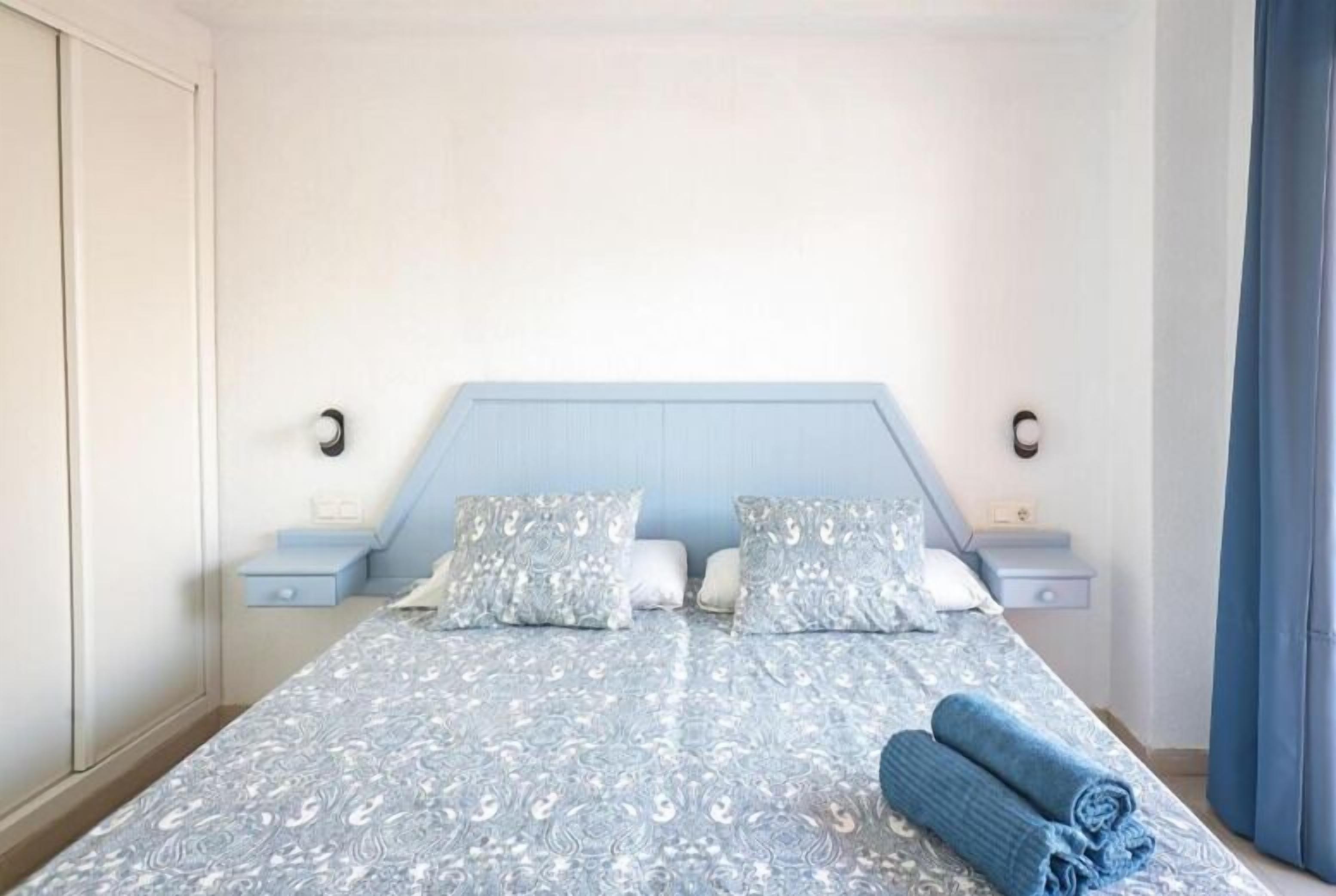 Ein Schlafzimmer mit einem Bett, Kissen, einem Nachttisch und einem zusammengerollten Handtuch.