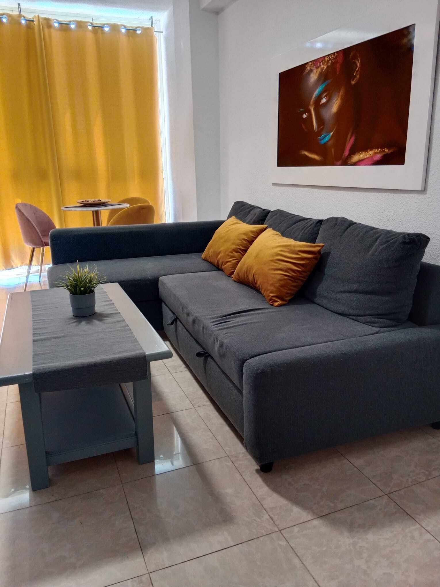 Ein modernes Wohnzimmer mit einer grauen Eckcouch, einem kleinen runden Tisch und einer Topfpflanze.
