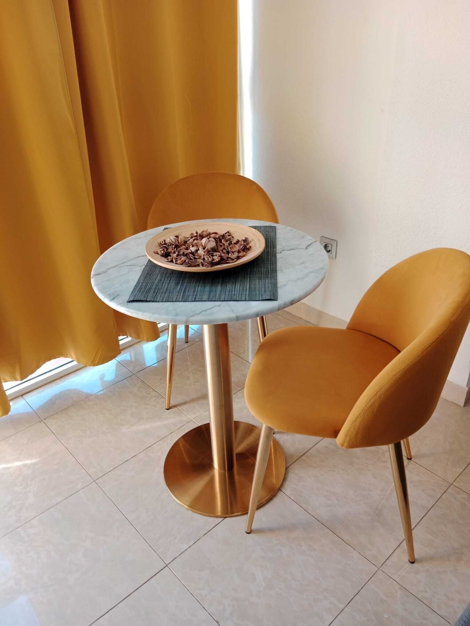 A dining area with a round table, two chairs, a plate of food, and a window with curtains.