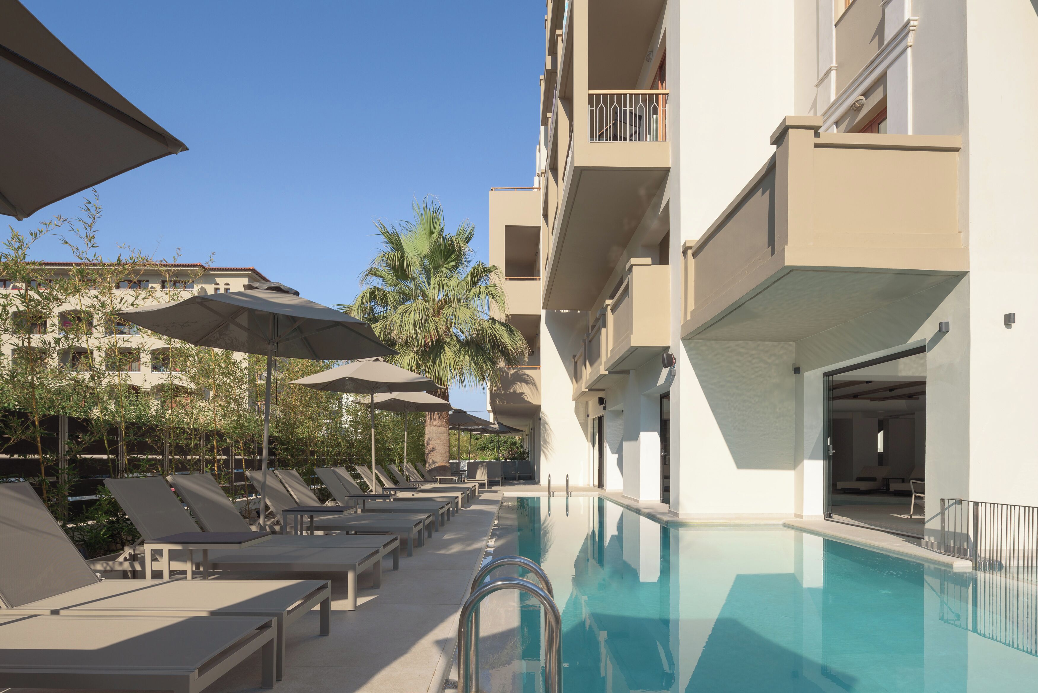 A poolside area with sun loungers, umbrellas, and a clear blue pool.