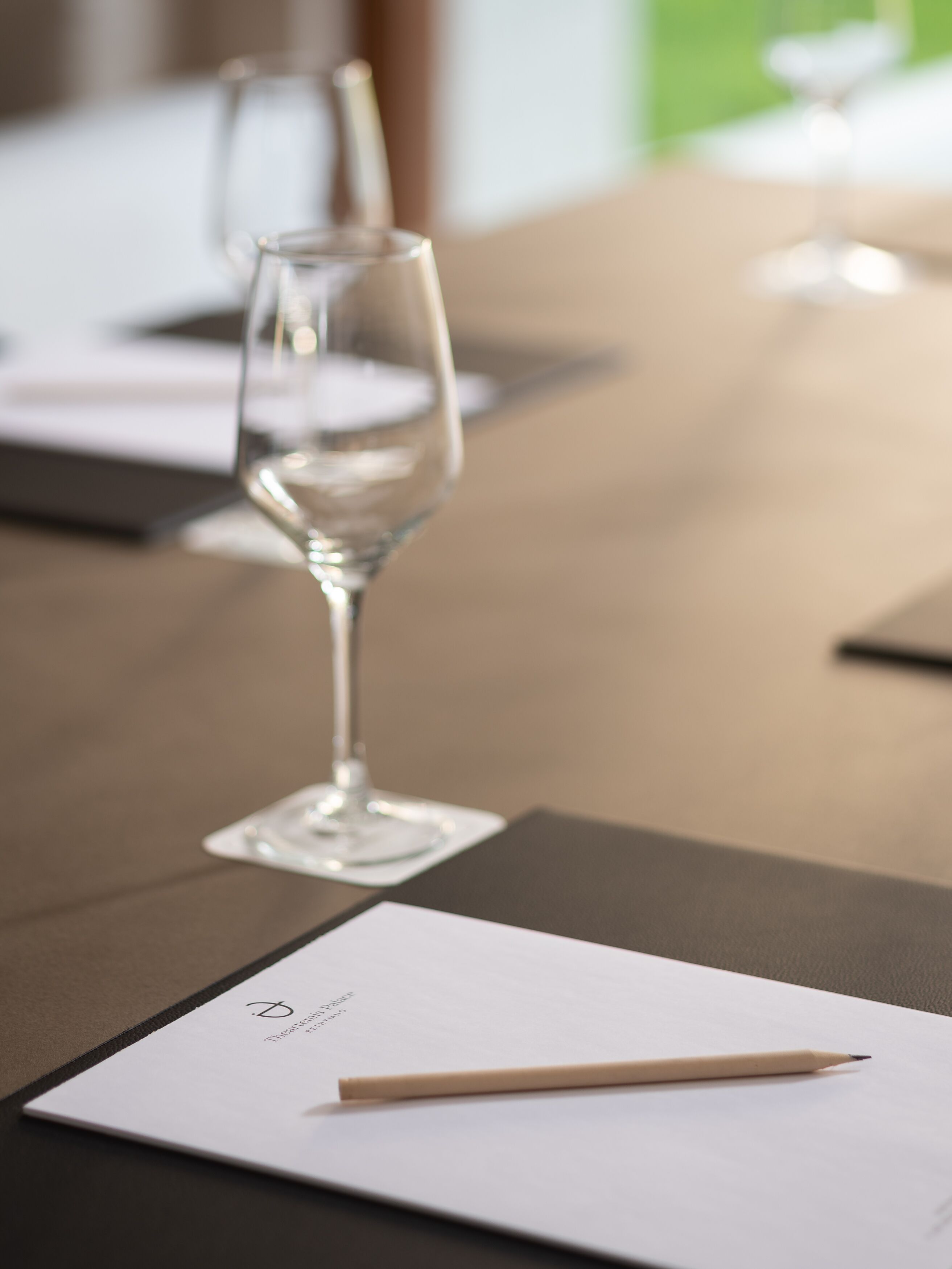 A conference table with a white placard and a pencil, and a clear glass wine glass in the background.