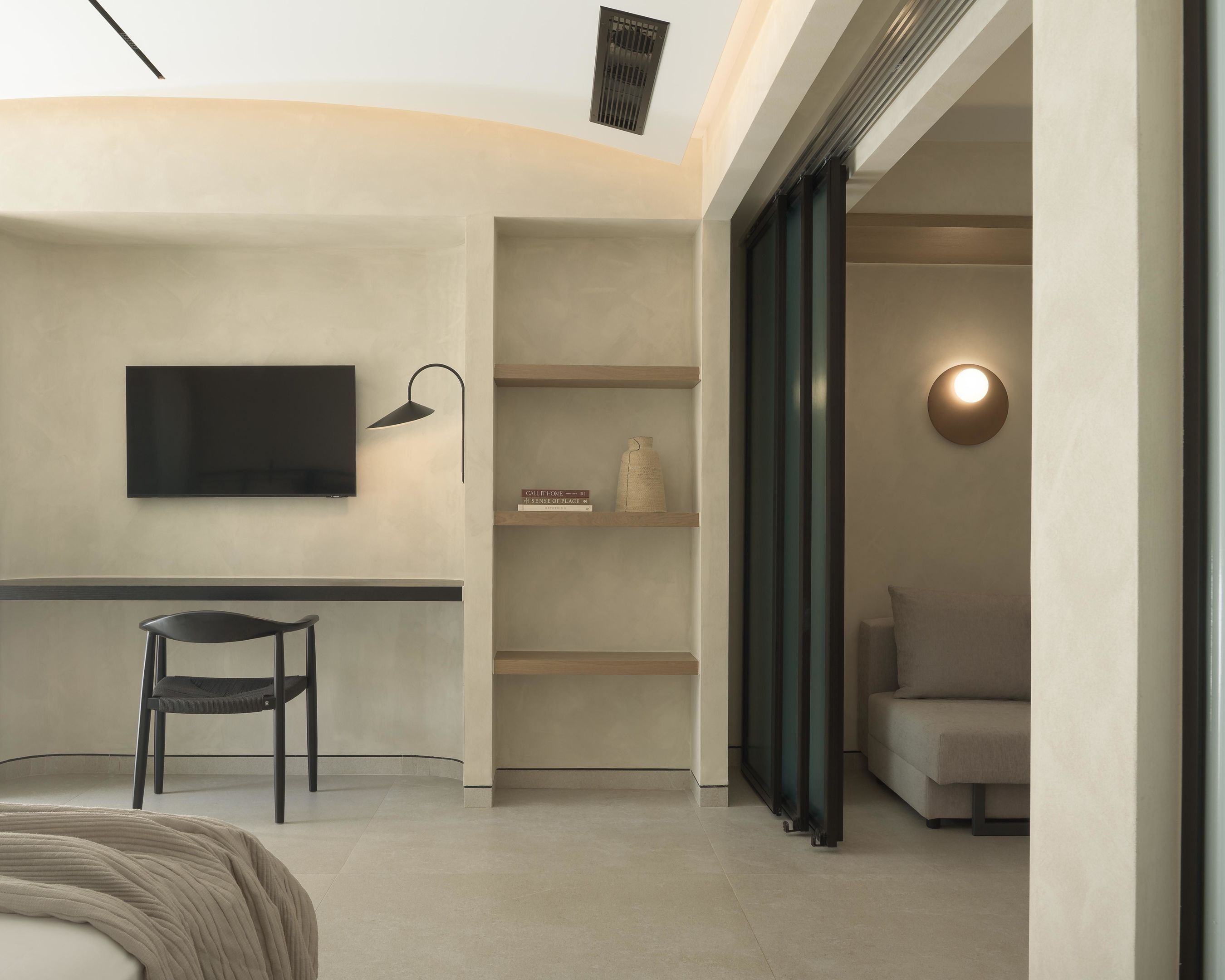 A modern room with a flat-screen TV mounted on the wall, a desk with a chair, a bookshelf, and a sofa.