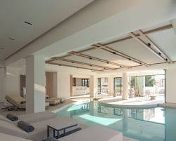 Piscina interior moderna con zonas de descanso, una cocina al fondo y amplios ventanales que permiten la entrada de luz natural.