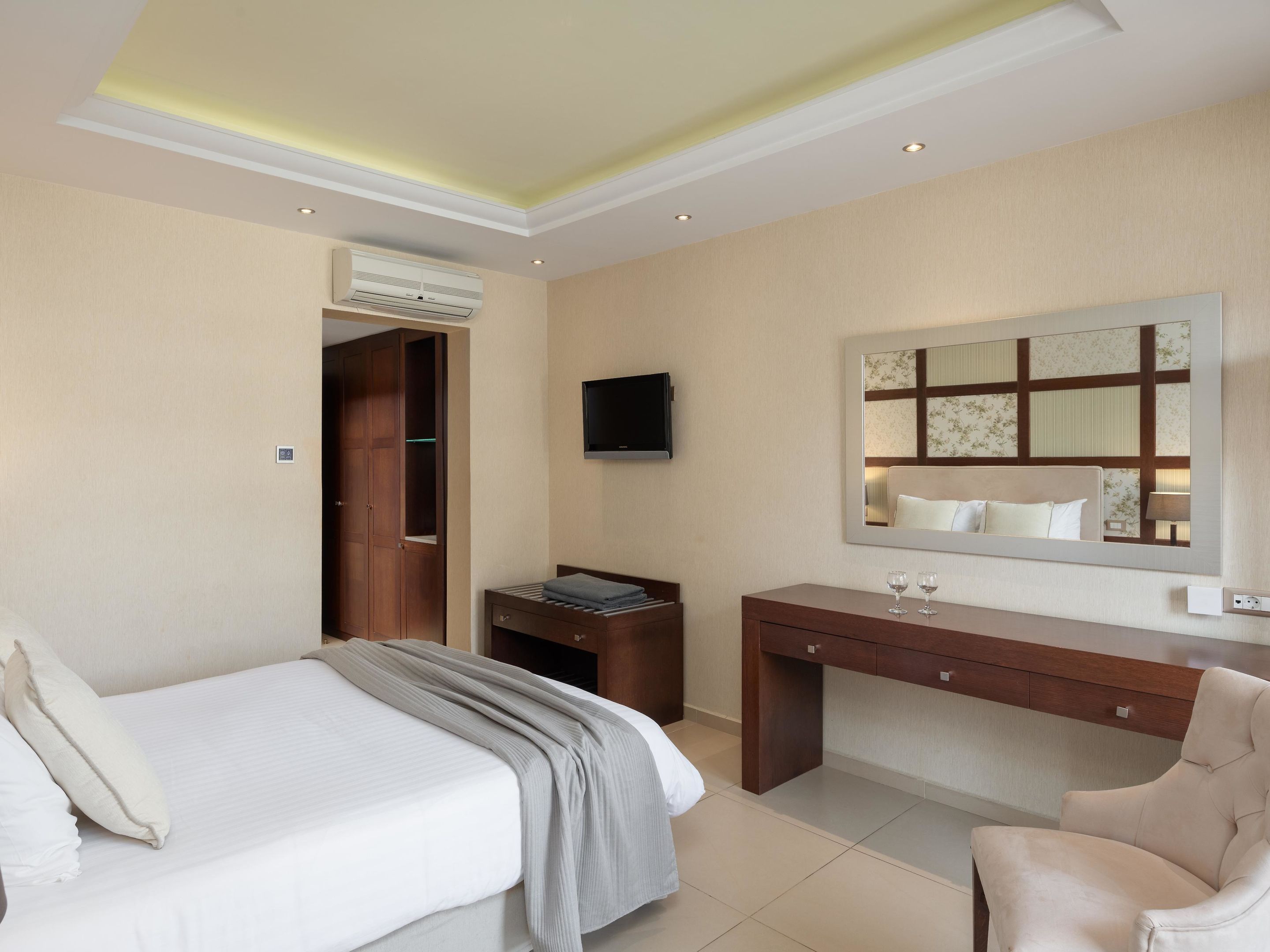A hotel room with a bed, a desk, a chair, a television, and an air conditioning unit.
