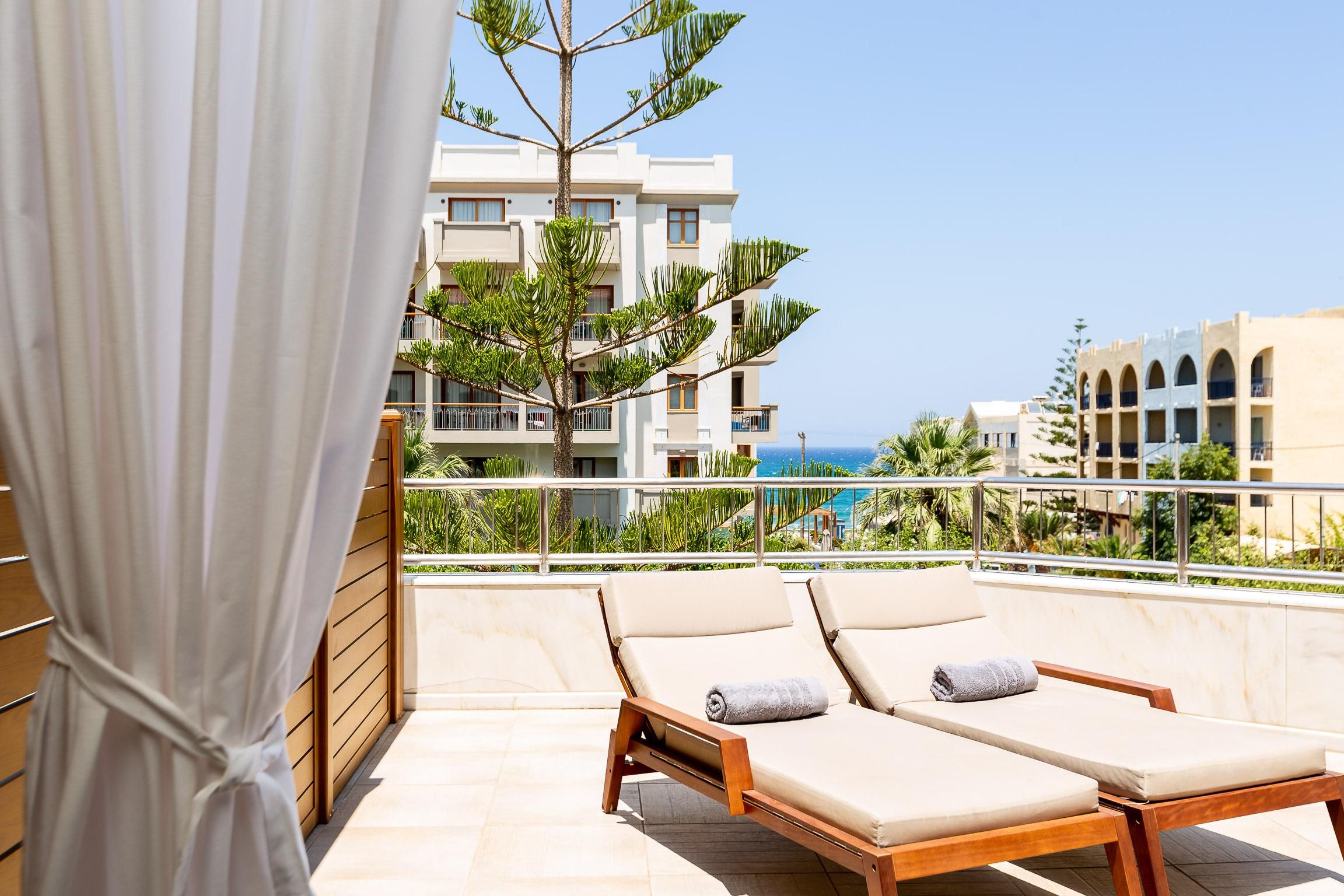 A balcony with two sun loungers, a wooden railing, and a view of a building with balconies and a clear sky.