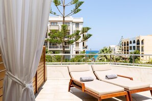 A balcony with two sun loungers, a wooden railing, and a view of a building with balconies and a clear sky. - Theartemis Palace (Rethymno)