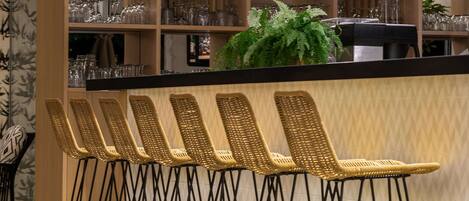 A bar area with wicker bar stools, hanging light fixtures, and shelves with glasses and bottles.