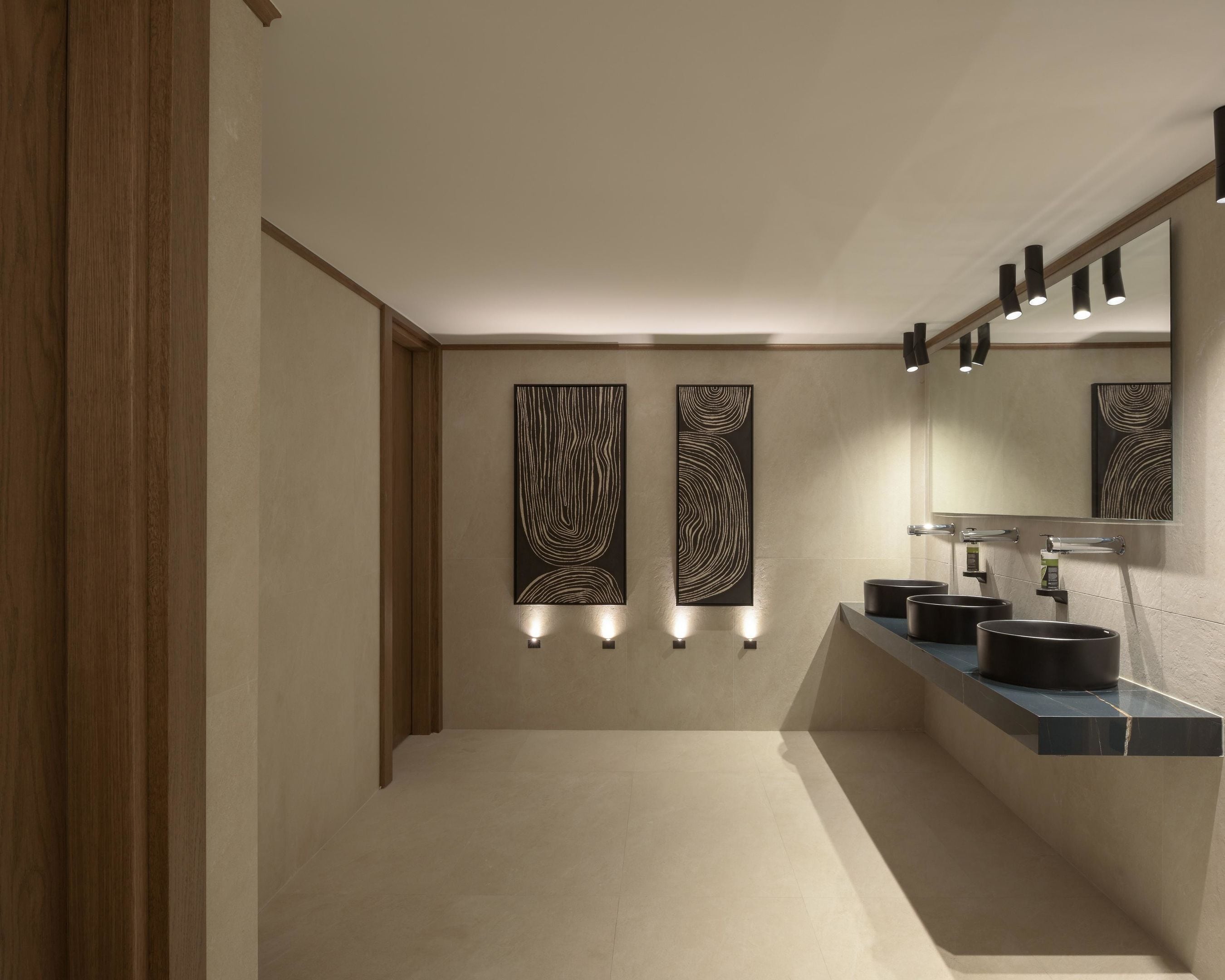A modern bathroom with a wooden door, a vanity with a mirror, and wall-mounted lights.