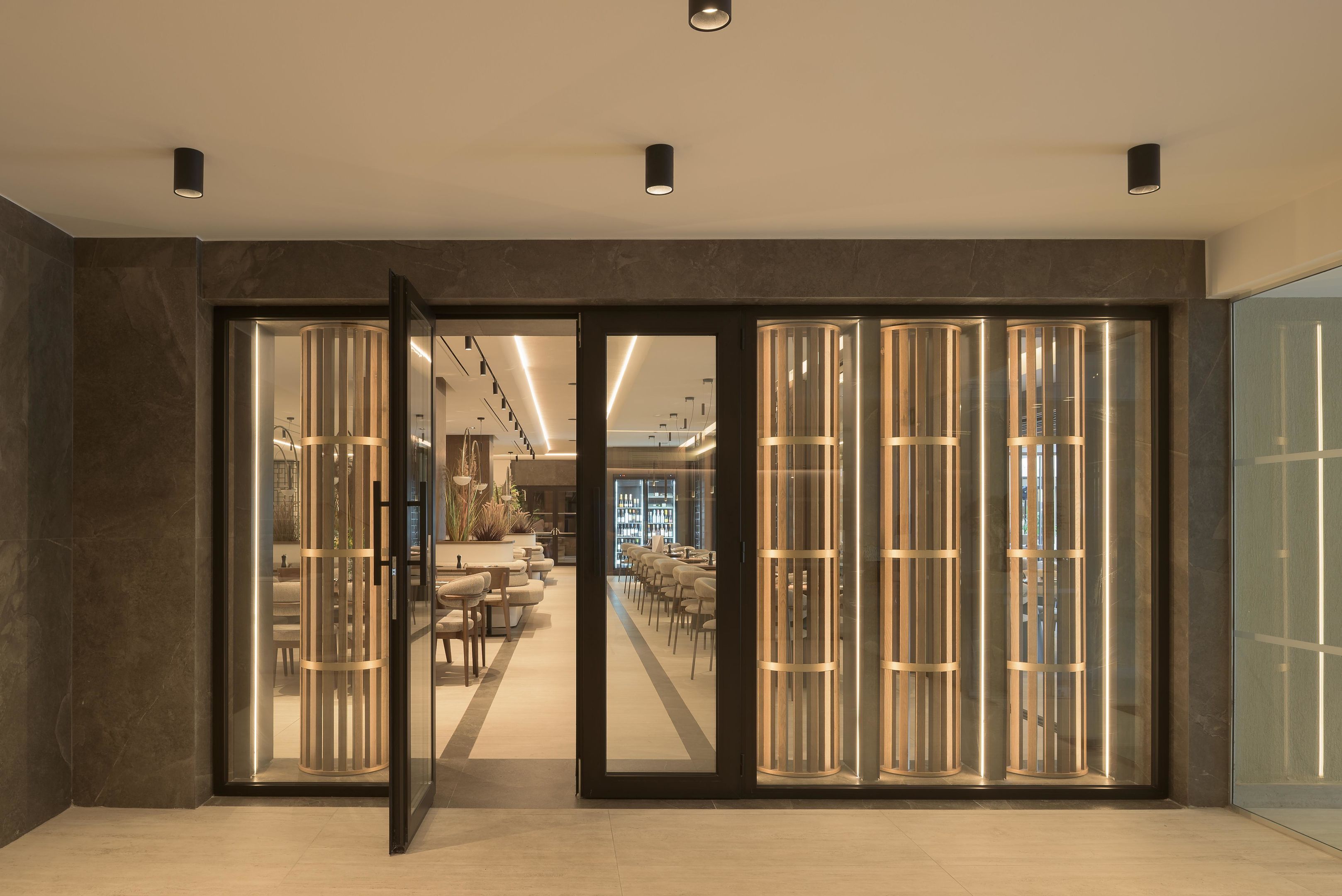 A modern interior with a glass door entrance, a seating area with tables and chairs, and a visible bar area in the background.